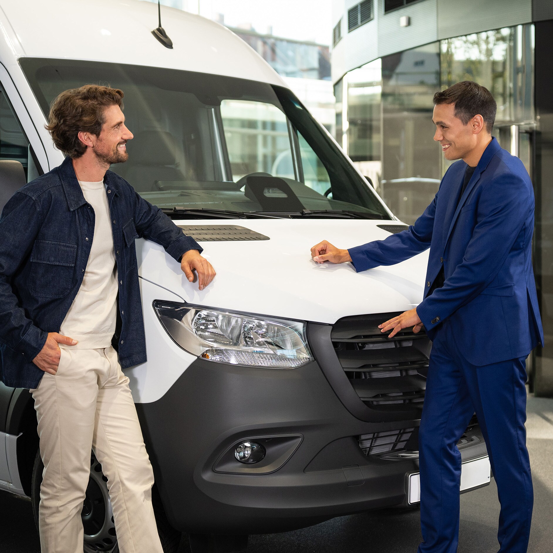 Oferta finansowania dla Twojego Mercedes-Benz Dwie osoby opierające się o samochód dostawczy Mercedes-Benz i prowadzące rozmowę.
