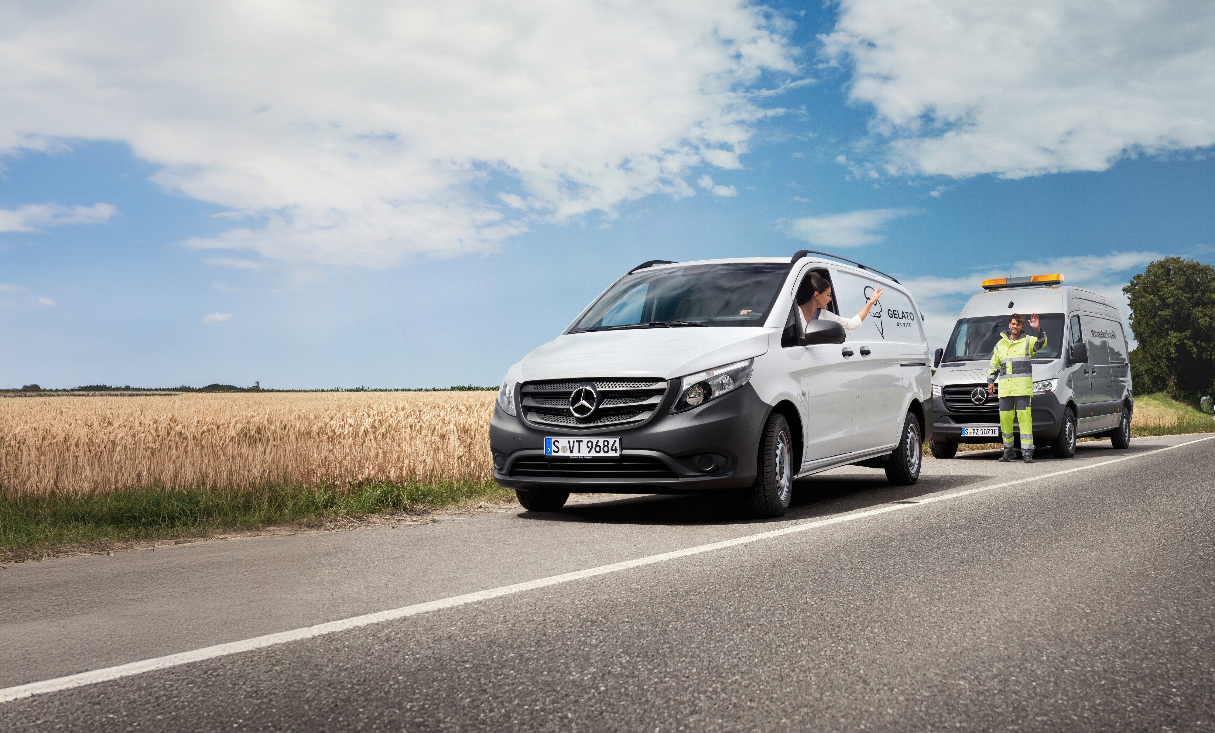 Service24h Mercedes-Benz Pracownik serwisu Mercedes-Benz pomaga kierowcy samochodu dostawczego na poboczu drogi, obaj machają w przyjazny sposób.