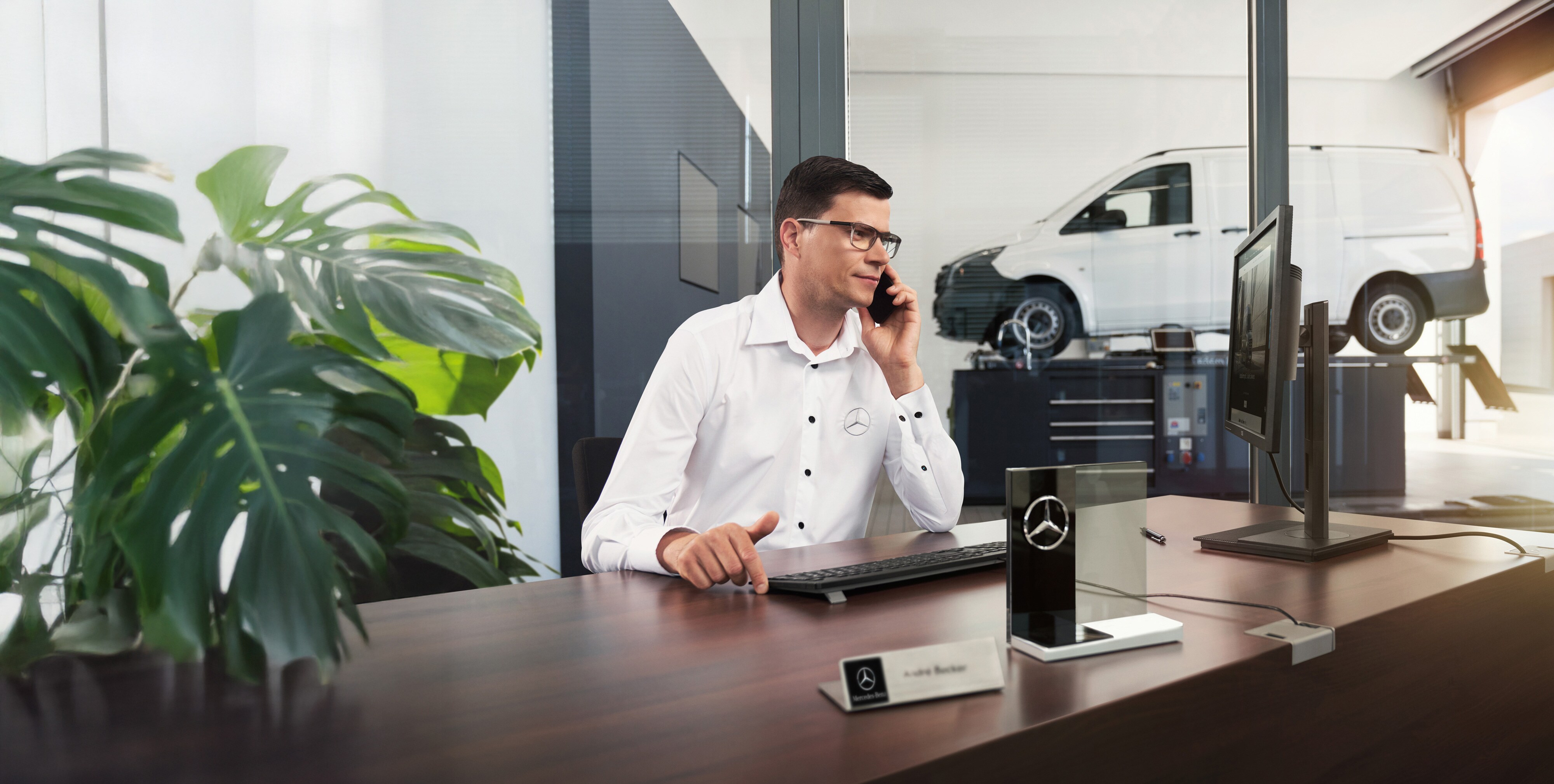 Eksperci pomocy drogowej Mercedes-Benz Pracownik Mercedes-Benz rozmawia przez telefon przy biurku z samochodem dostawczym Mercedes-Benz Vito w tle.