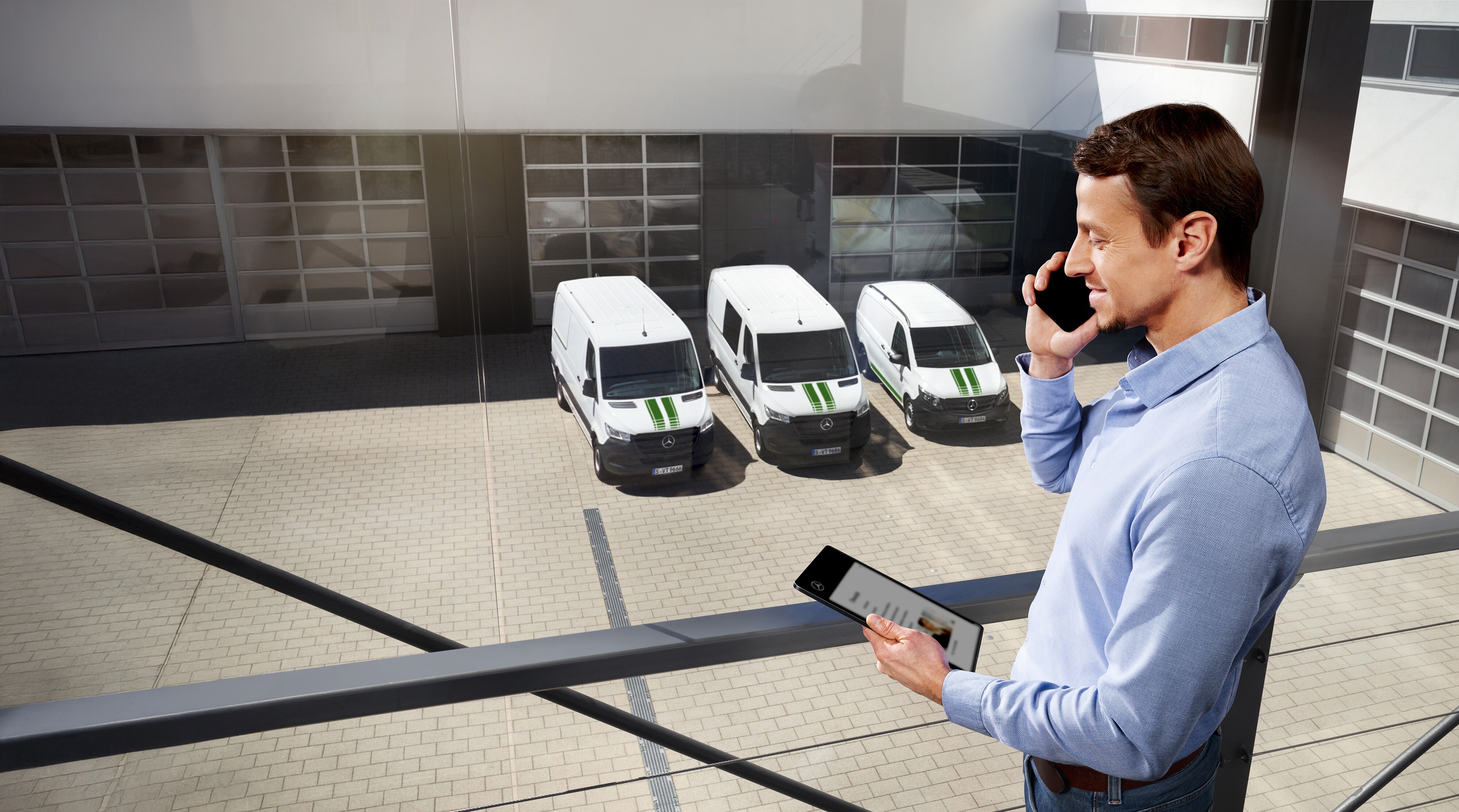 Gwarancja Mercedes-Benz | Samochody dostawcze Mercedes-Benz Mężczyzna rozmawiający przez telefon z tabletem w ręku stojący przed trzema samochodami dostawczymi Mercedes-Benz.