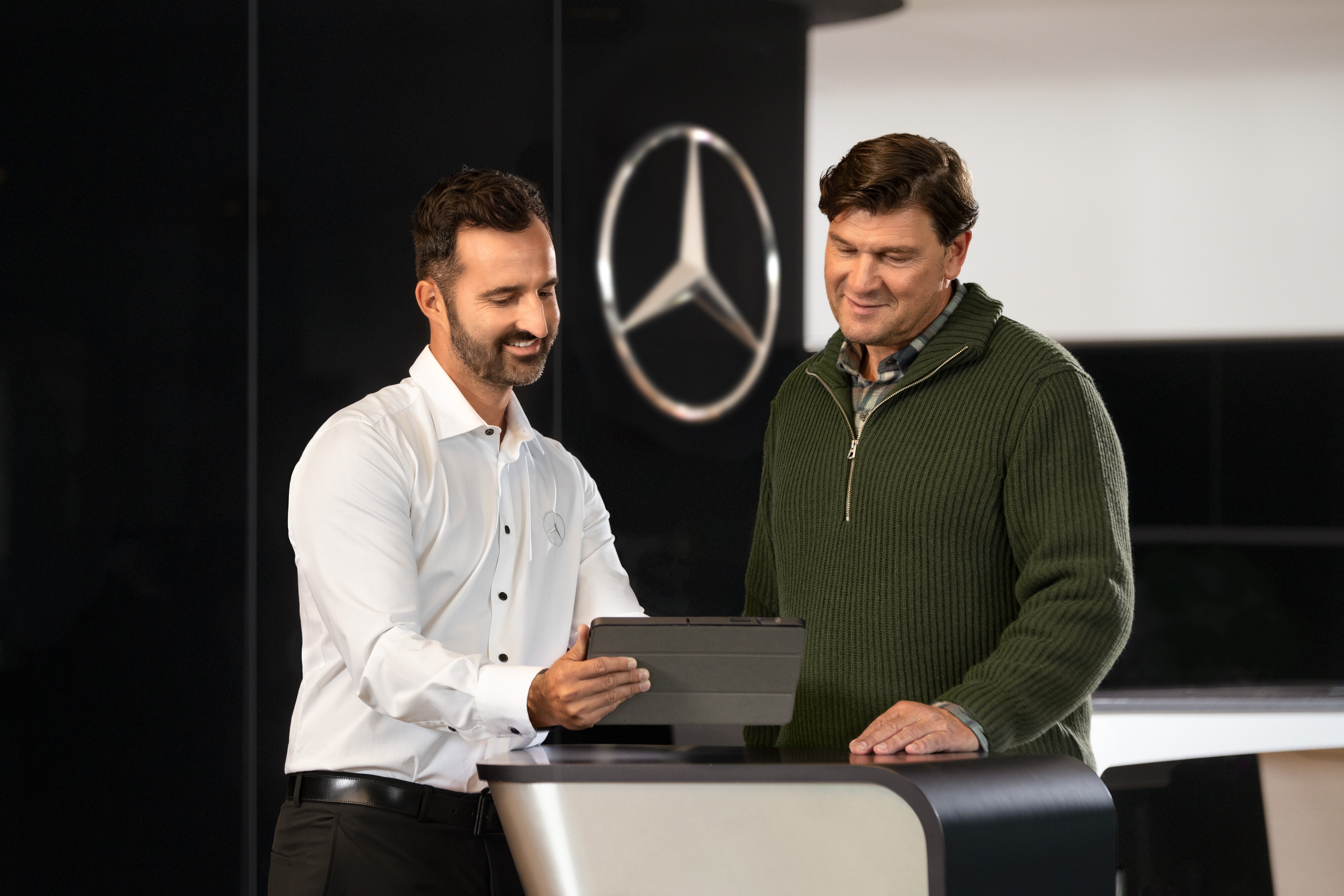 Mercedes-Benz | Przegląd Usług Dwóch mężczyzn rozmawia przy kontuarze, patrząc na tablet, przed gwiazdą Mercedes-Benz.