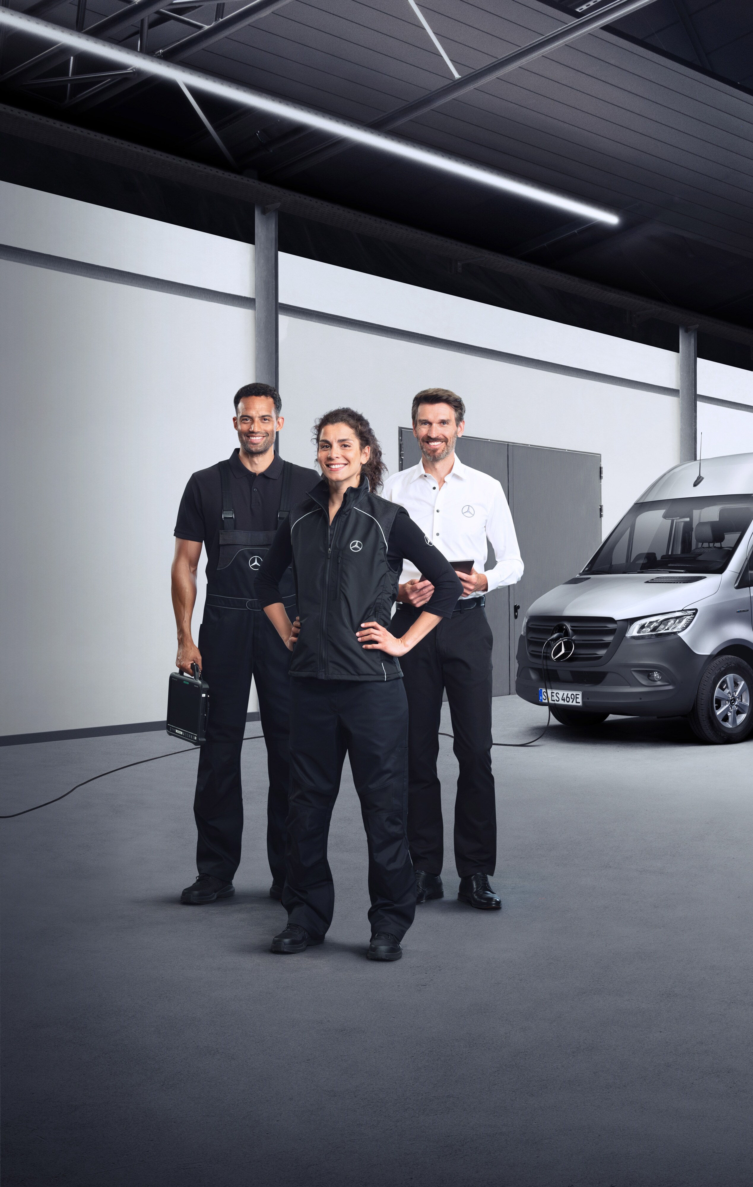 Mercedes-Benz | Przegląd Usług | Usługi dla Elektrycznych Samochodów Dostawczych Trzech pracowników stoi przed srebrnym samochodem dostawczym Mercedes-Benz eSprinter z podłączonym przewodem do ładowania.