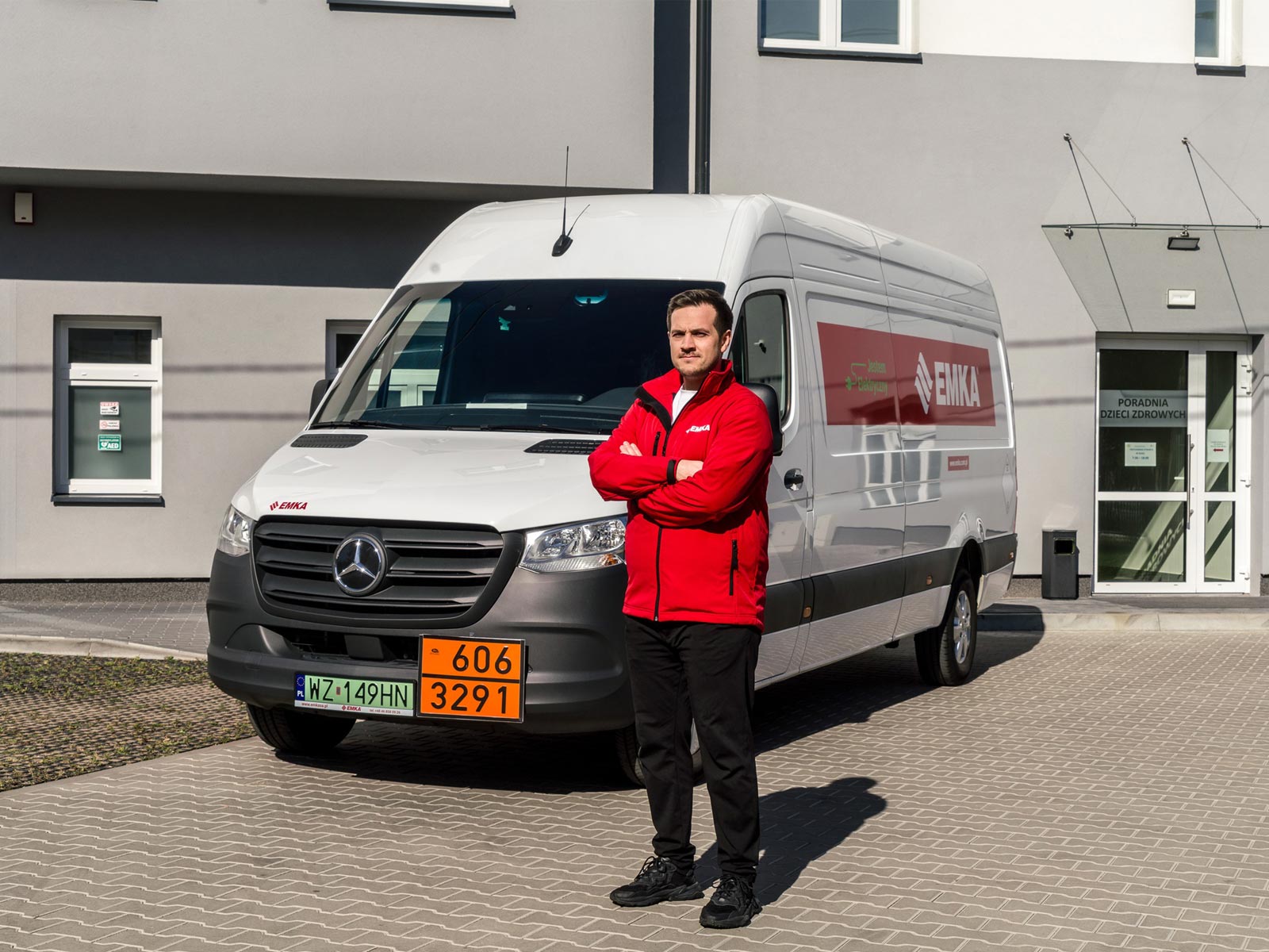 eSprinter w Emka S.A. – zielony transport odpadów medycznych Mężczyzna w czerwonej bluzie stoi przed białym Mercedesem eSprinter.