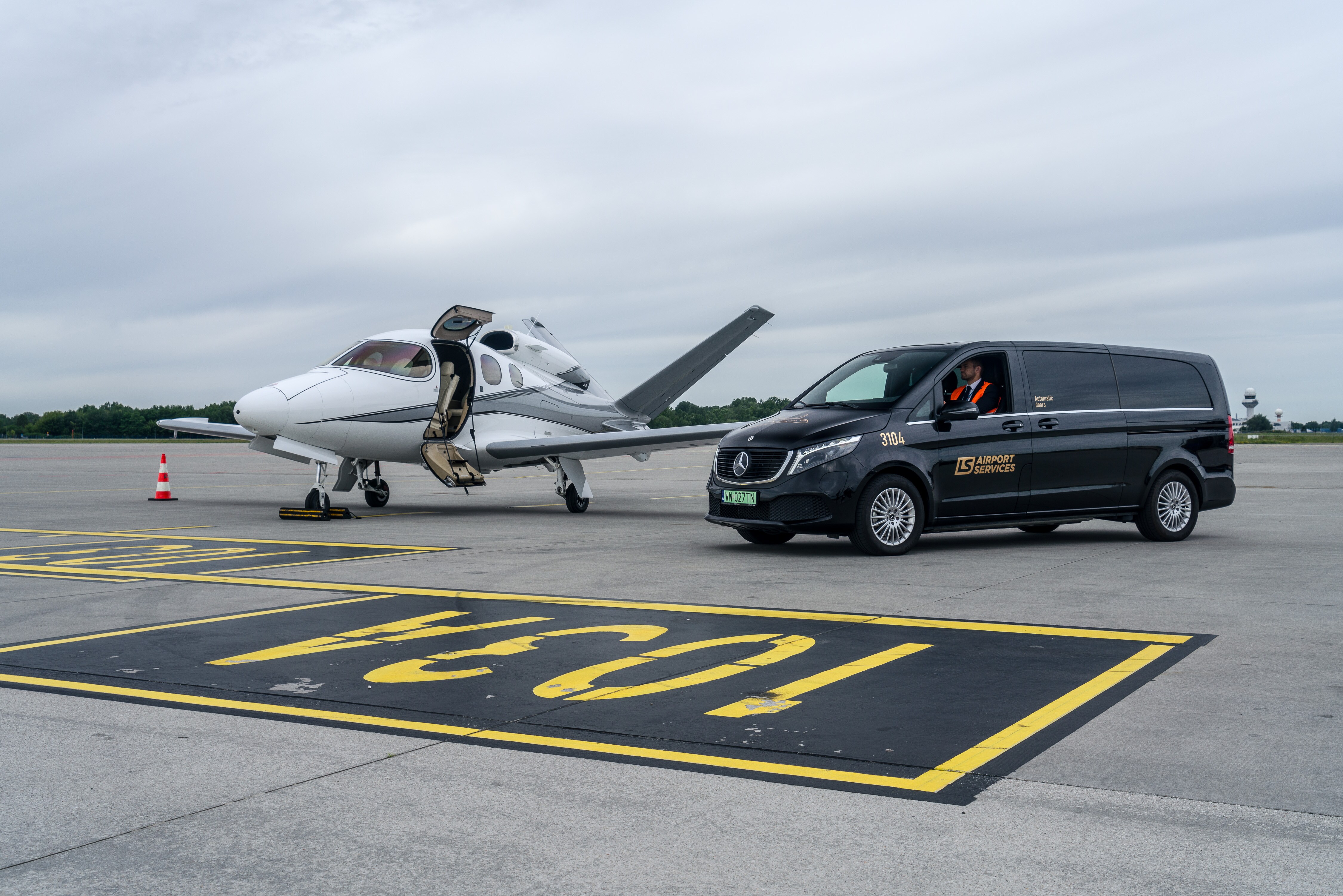 Mercedes-Benz EQV w LS Airport Service: czysty komfort na Lotnisku Chopina Czarny Mercedes EQV na płycie lotniska obok prywatnego odrzutowca.